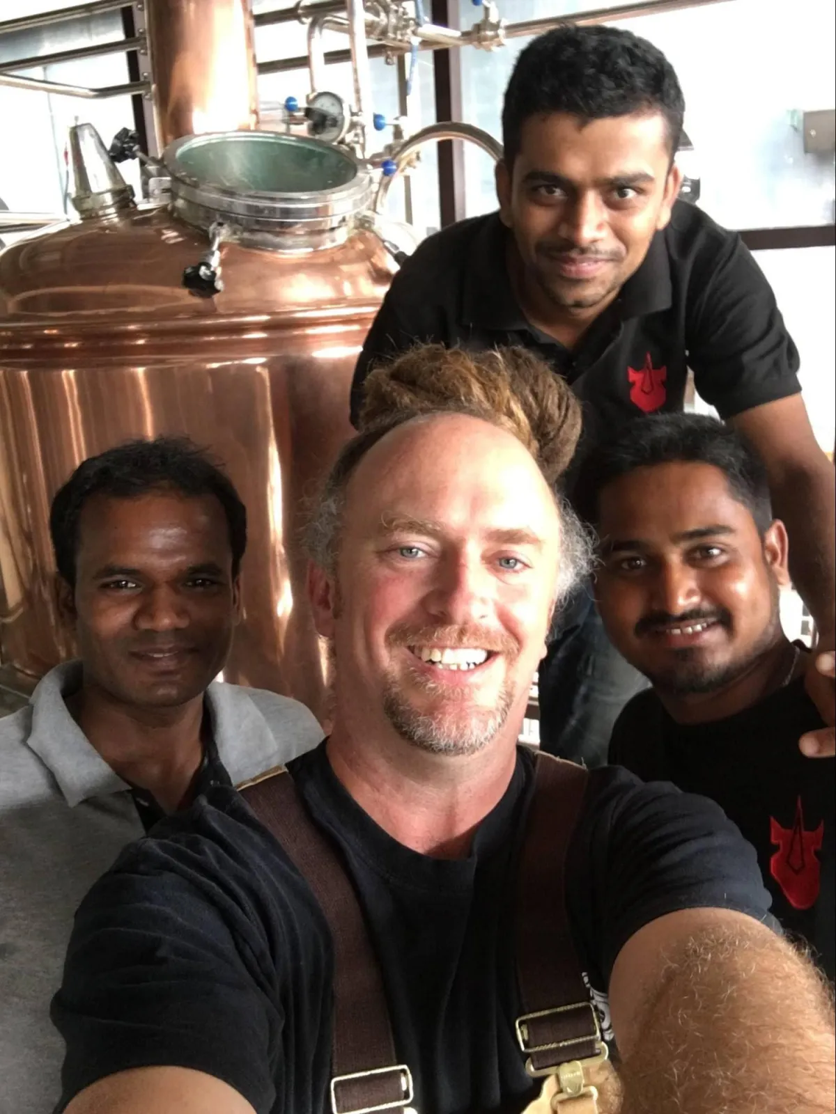 Daniel with a brewery crew beside a copper brewhouse